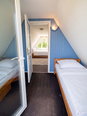 Ein Schlafzimmer mit zwei Einzelbetten, einer Tür zu einem anderen Raum und einem Fenster, das für natürliches Licht sorgt.