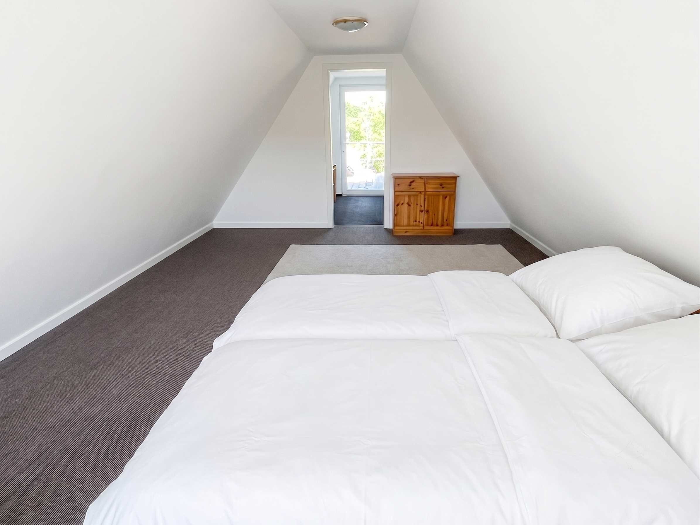 A bedroom with a bed, a wooden cabinet, and a view of the outdoors through a door.