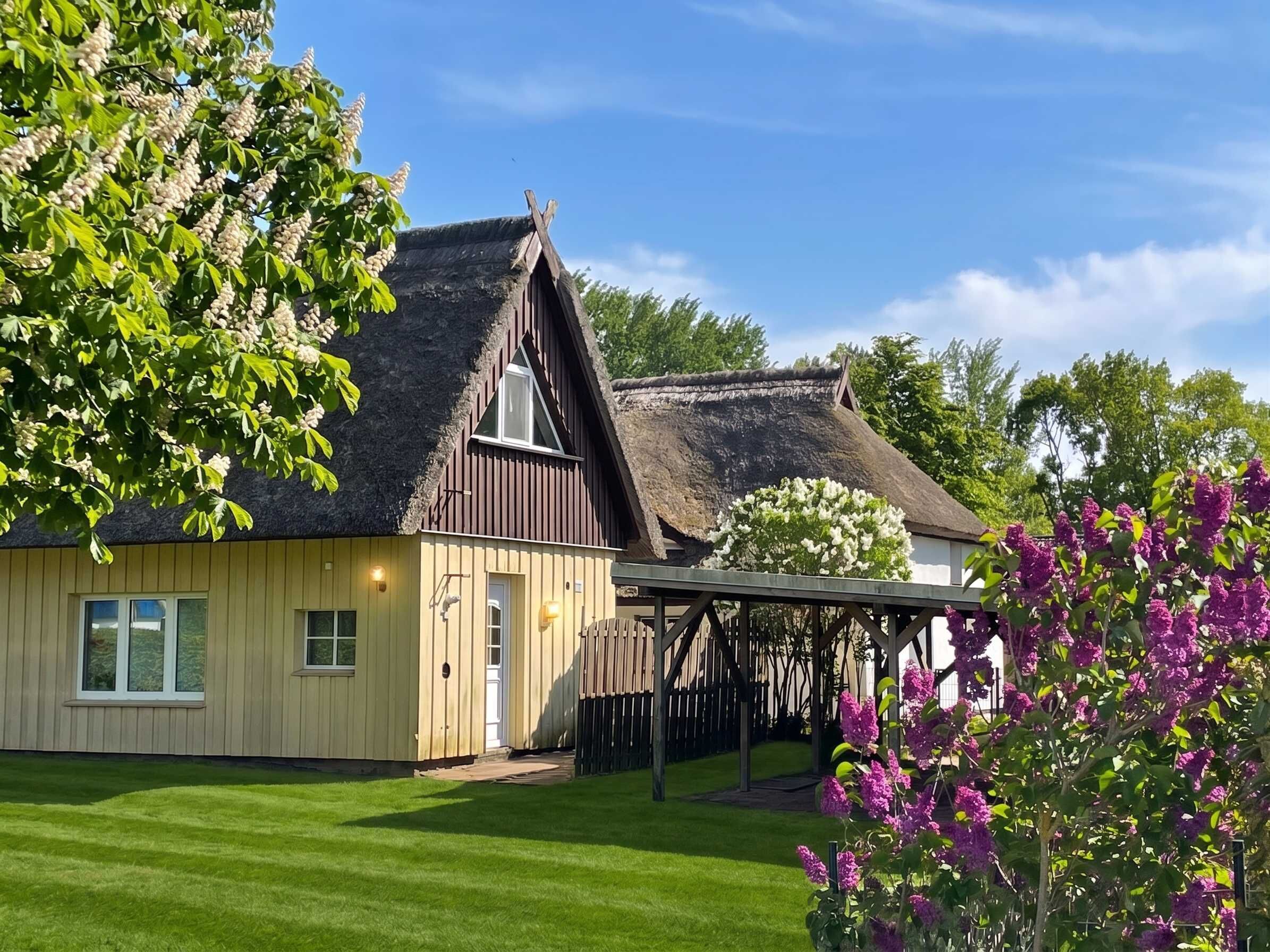 A traditional wooden house with a thatched roof, a fenced yard, and a well-maintained lawn.