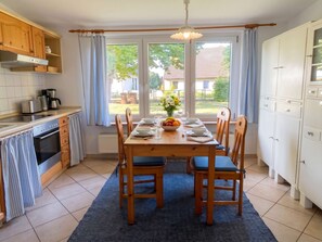 Eine moderne Küche mit Esstisch für vier Personen, einem eingebauten Backofen und Blick auf eine Wohngegend durch große Fenster.