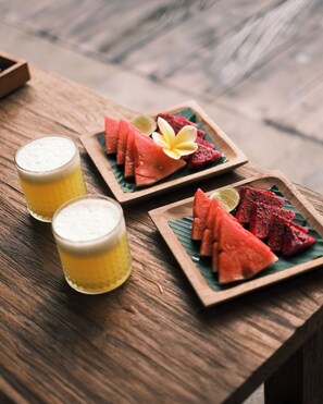Una mesa de madera con dos vasos de una bebida amarilla y dos platos de madera con sandía y una cuña de lima.