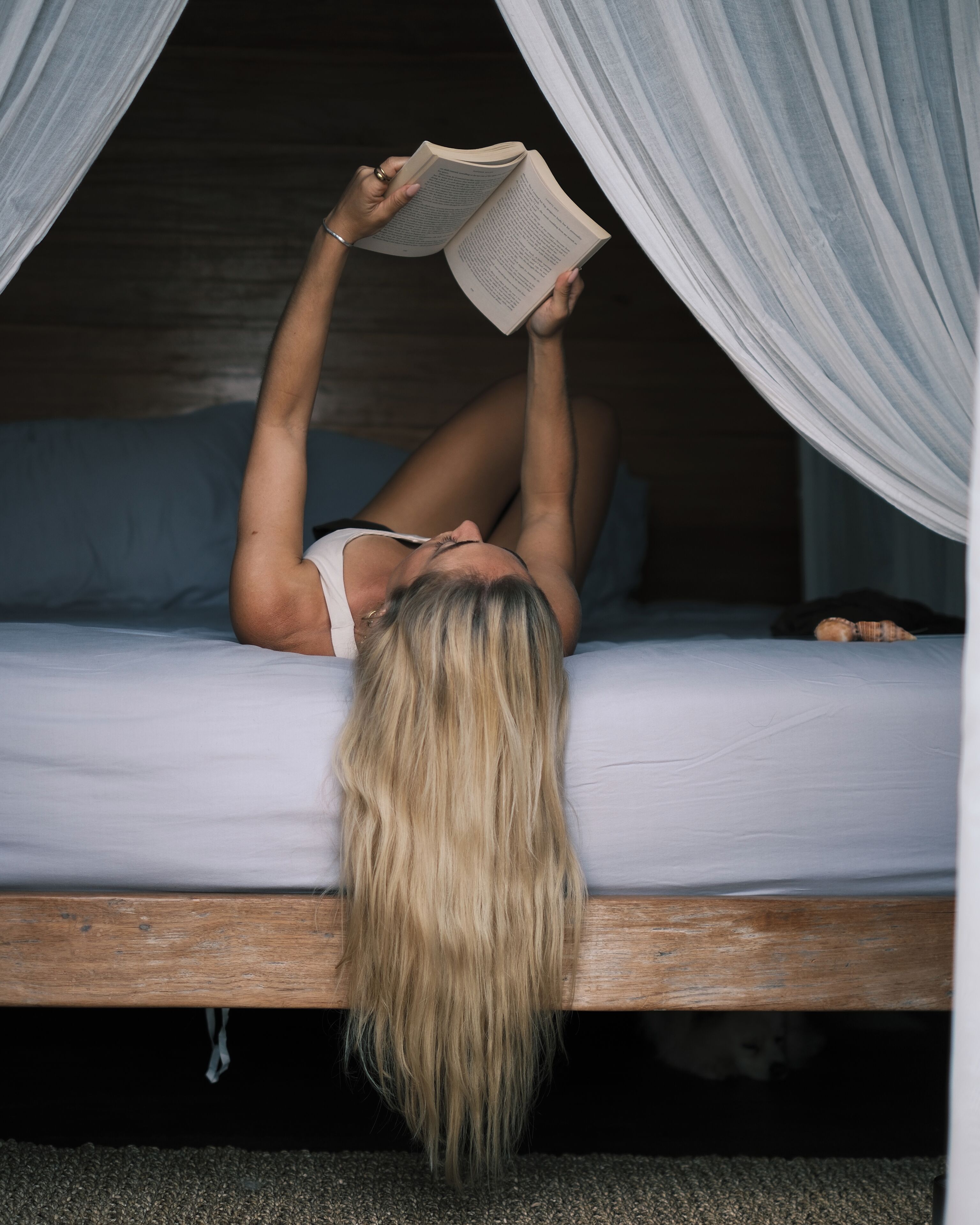 Une personne allongée sur un lit, un livre à la main, sous un dais.