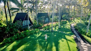 A tropical resort with thatched-roof cottages, a well-maintained lawn, and a stone pathway. - Desa Cabins (Tabanan)
