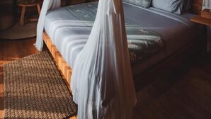 A room with a bed under a canopy, wooden walls, and a small table with a plant. - Desa Cabins (Tabanan)