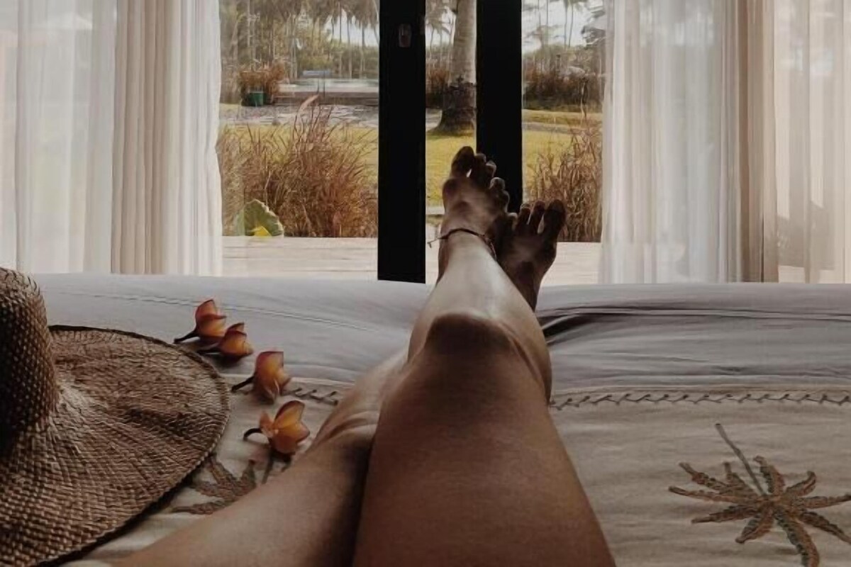 Una habitación con una cama, vista a palmeras a través de una ventana y ambiente tropical.
