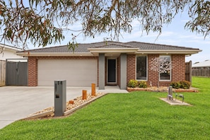 A single-story house with a garage, a front door, and a small front yard with a tree and shrubs. - The Grampian by Ready Set Stay (Cowes)