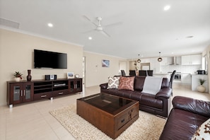 Ein modernes Wohnzimmer mit Flachbildfernseher, einer dunkelbraunen Unterhaltungseinheit, einer Ledersofa und einem Glastisch.