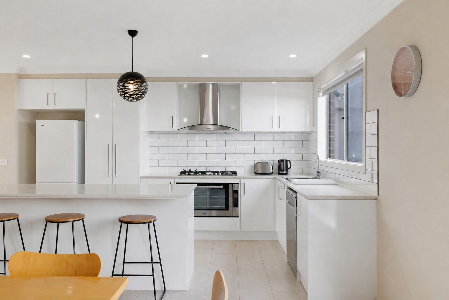 A modern kitchen with white cabinetry, a central island with stools, a gas stove, an oven, and a window with a view.