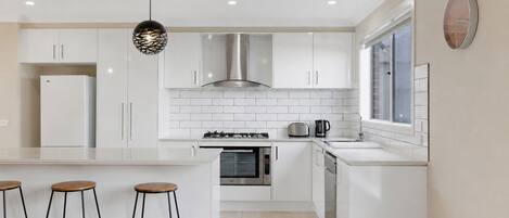 A modern kitchen with white cabinetry, a central island with stools, a gas stove, an oven, and a window with a view.