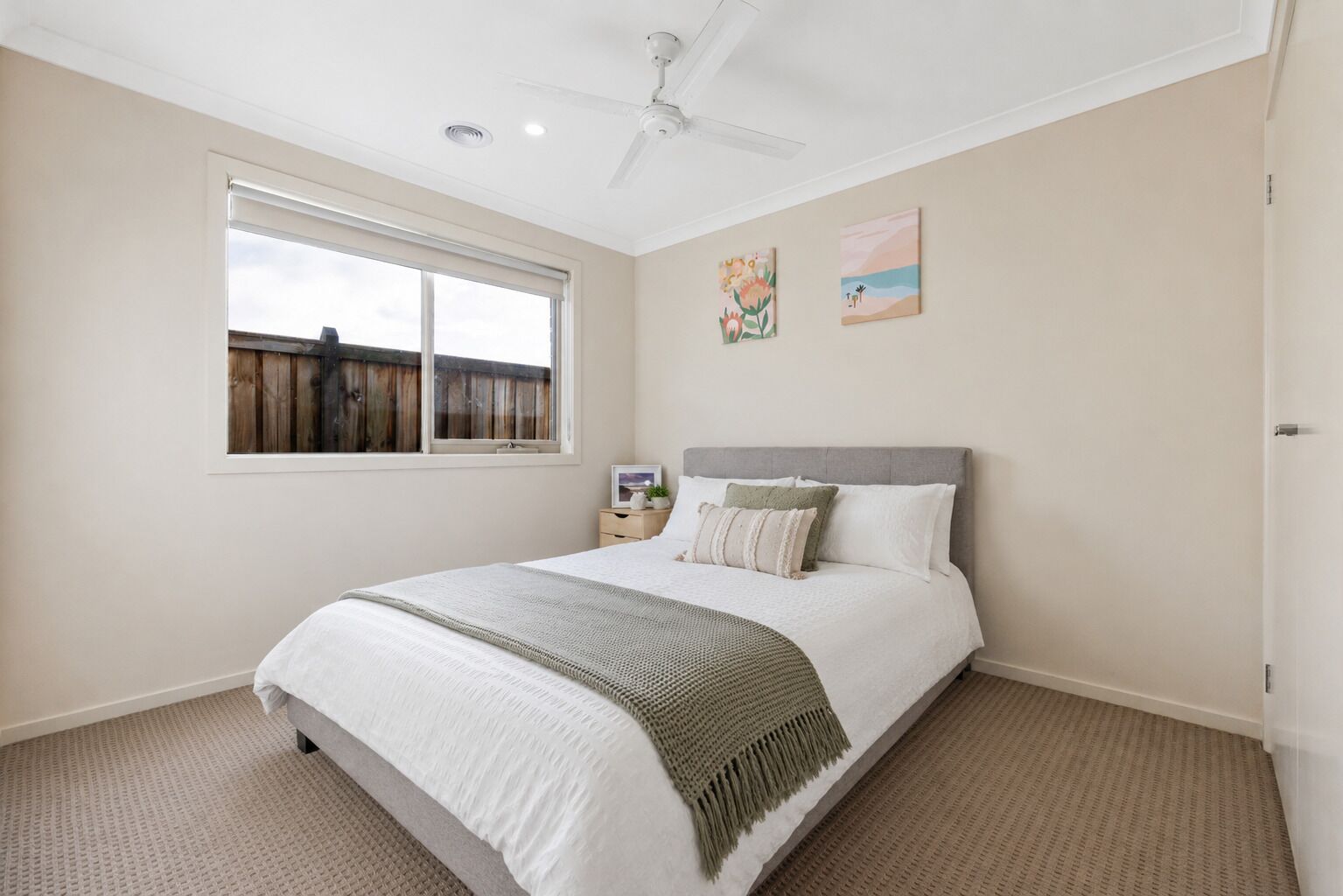 Un dormitorio con cama, ventilador de techo, ventana y obras de arte en la pared.