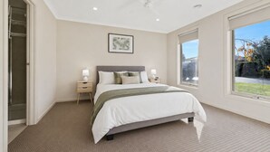 Une chambre à coucher avec un lit, des tables de chevet, un ventilateur de plafond, une fenêtre et un tableau encadré au mur.