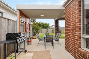Eine Terrassengruppe im Freien mit Grill, Sitzgelegenheiten und Blick auf den Garten.