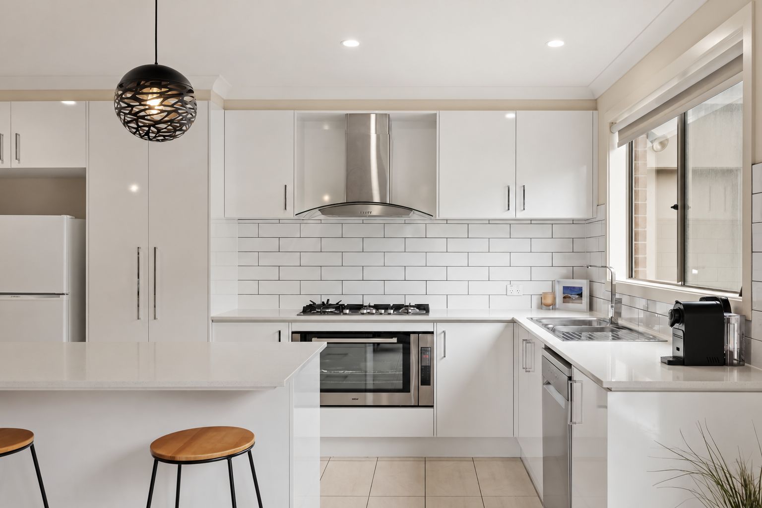 A modern kitchen with white cabinetry, stainless steel appliances, and a central island with stools.