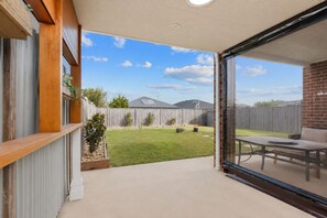En overdækket terrasse med udsigt til en baghave, en træterrasse og en murstensmur.