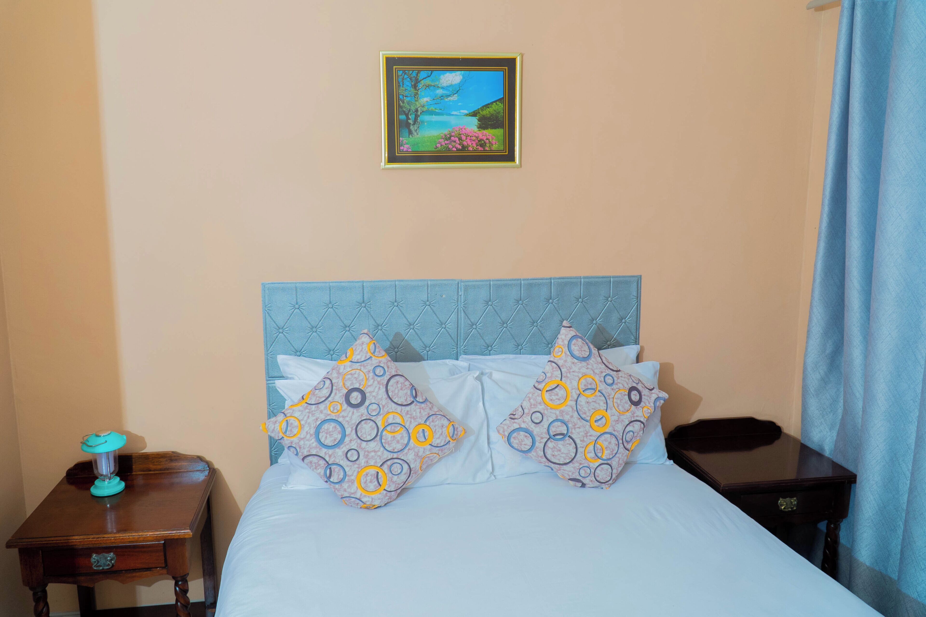 A bedroom with a bed, two pillows, a nightstand, a picture frame, and a curtain.
