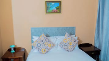 A bedroom with a bed, two pillows, a nightstand, a picture frame, and a curtain.