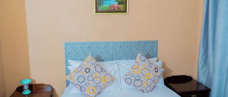 A bedroom with a bed, two pillows, a nightstand, a picture frame, and a curtain.