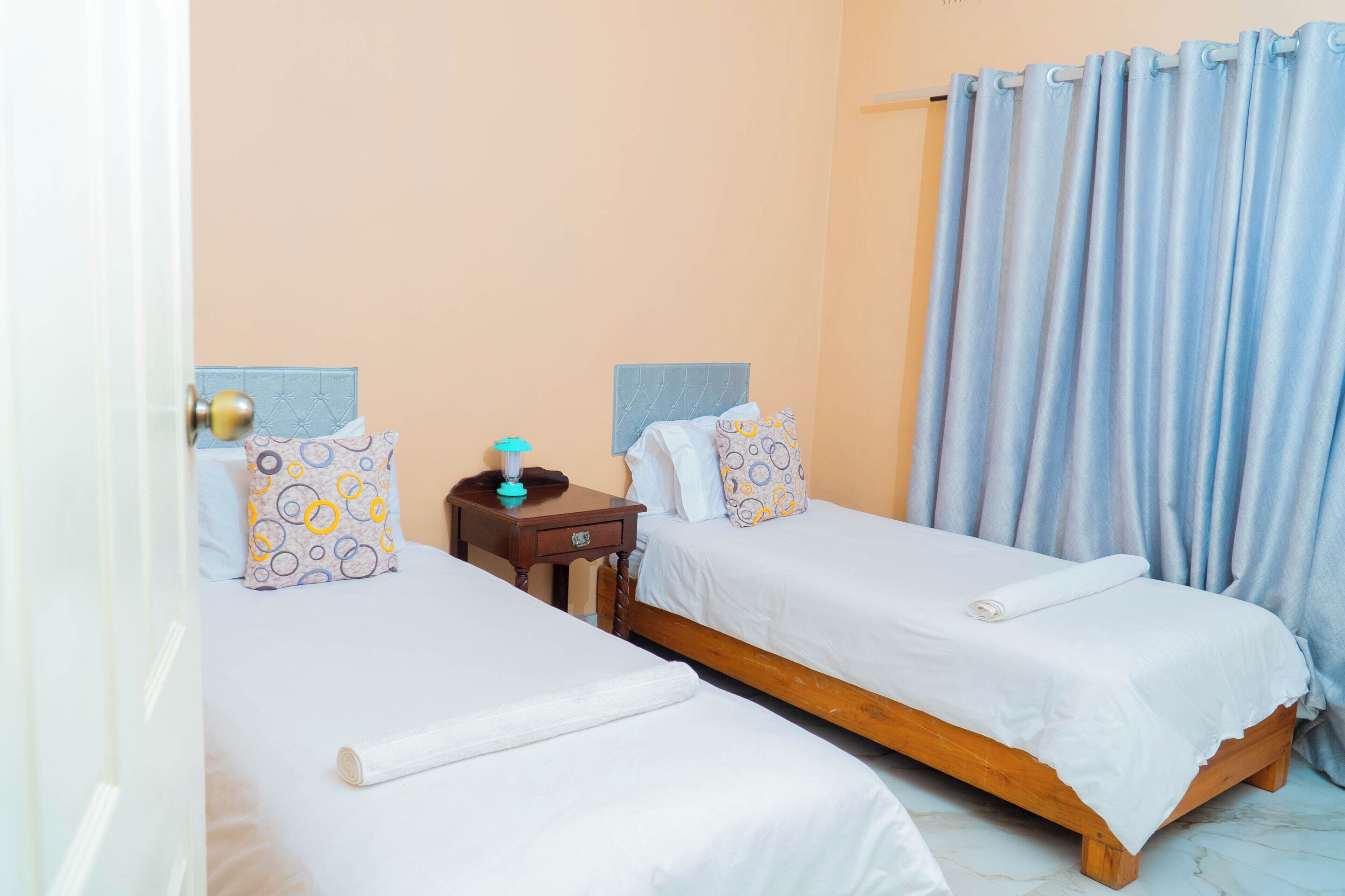 A room with two single beds, a bedside table with a lamp, and a curtain.