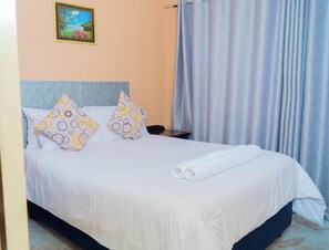 A neatly made bed with a white duvet and two patterned pillows, a headboard, a nightstand, and a framed picture on the wall.