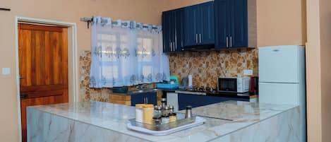 A kitchen with a marble island, blue cabinets, a refrigerator, and a microwave.