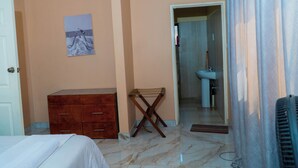 A hotel room with a bed, a wooden dresser, a folding chair, a bathroom with a sink, and a shower.