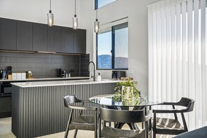 Et moderne køkken med en central ø, mørke skabe og hængende lamper.
