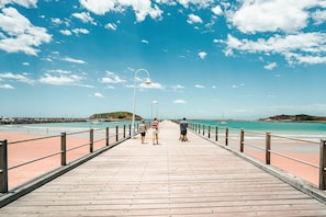 A wooden pier extending into a beach with clear skies and calm waters.