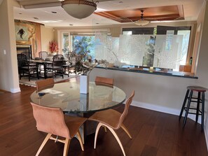 A dining area with a glass table surrounded by chairs, a kitchen area with a countertop, and a view of the outdoors.