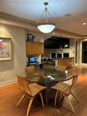 A modern dining area with a glass table, wooden chairs, and a pendant light. - Vancouver West Hillside Villa  4BR Panoramic Views (Vancouver)