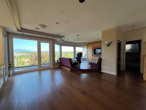 A spacious living room with large windows, a flat-screen TV, and a massage chair.