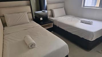 A hotel room with two beds, a nightstand, and a window with a view of buildings.