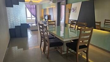 A modern dining area with a glass table and wooden chairs, a television, and a view into the living area.