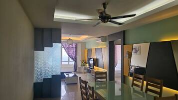 A modern living room with a glass dining table, a ceiling fan, and a TV.
