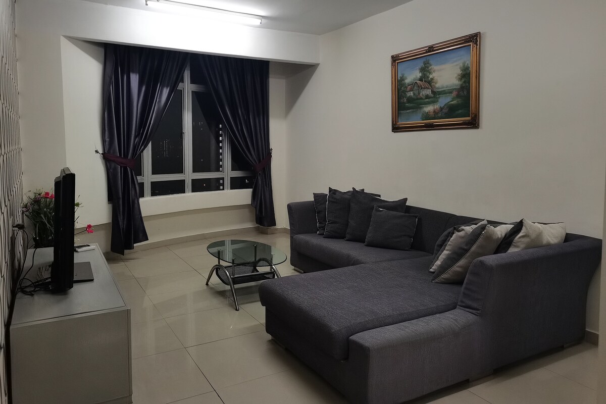 A living room with a grey sofa, a glass coffee table, a painting on the wall, and a window with curtains.