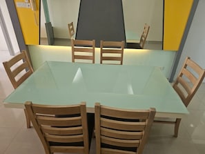 A dining table with four wooden chairs, a glass top, and a yellow wall in the background. - Putra Majestik Manage By City Haven (Jalan Ipoh)