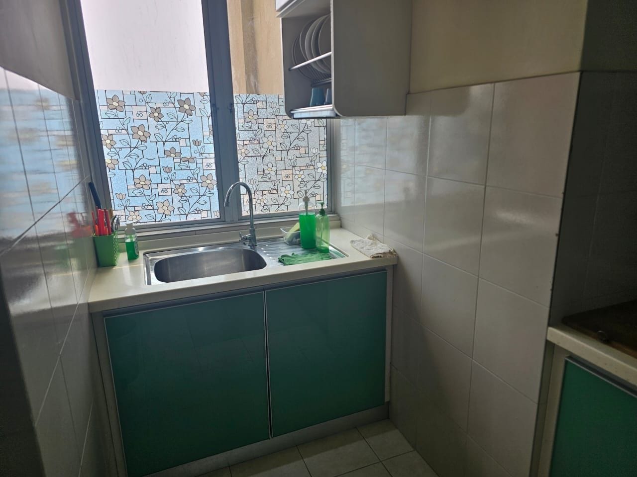 A kitchen with a sink, green cabinets, and a tiled backsplash.