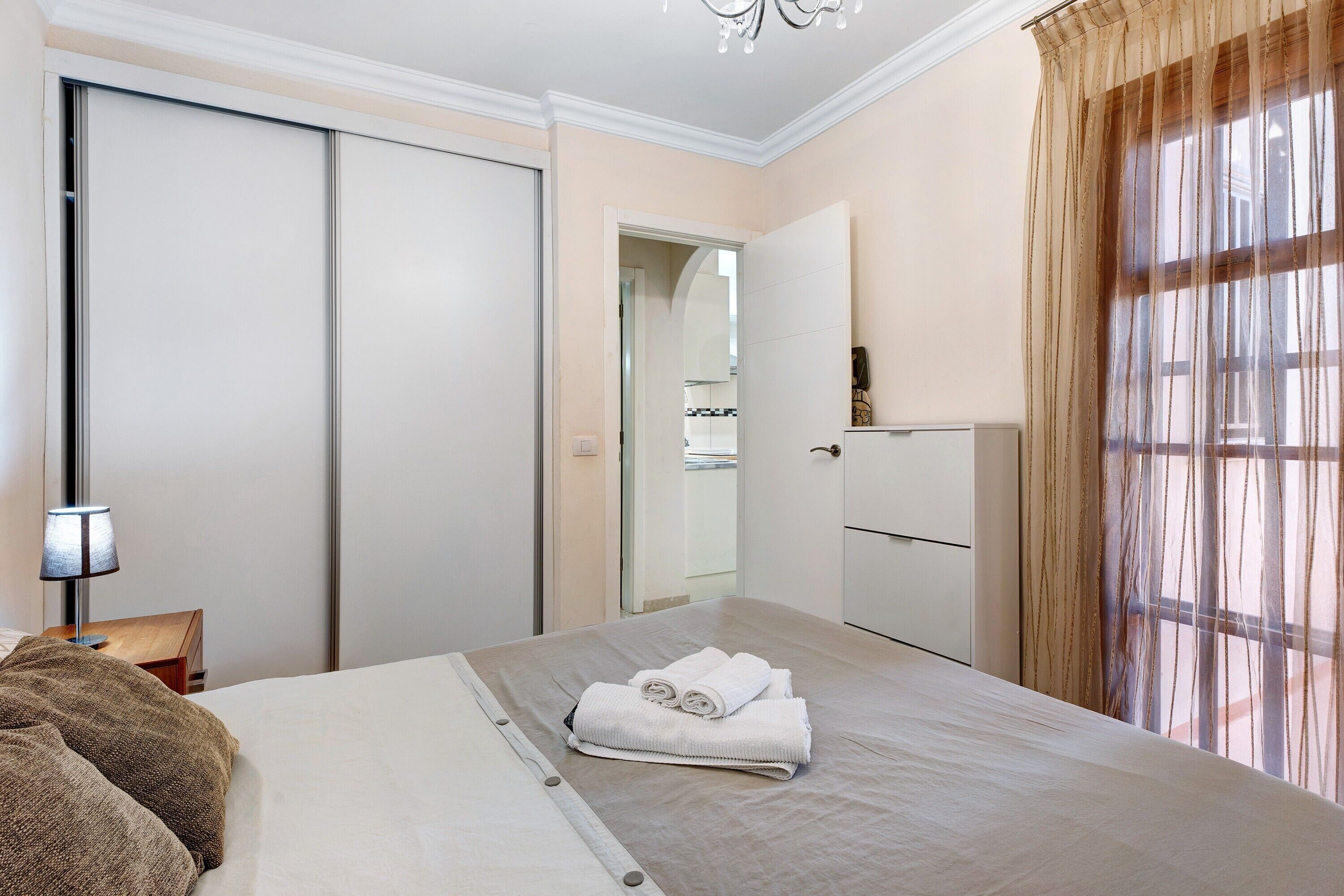Ein Hotelzimmer mit Bett, Nachttisch, Lampe, Kleiderschrank und Spiegel.