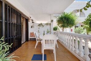 Eine Terrasse im Freien mit Tisch und Stühlen, umgeben von Kübelpflanzen und einem weißen Geländer.