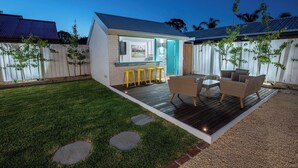 A small house with a deck, outdoor seating, and a TV mounted on the wall. - Ocean Breeze Retreat (Ocean Grove)