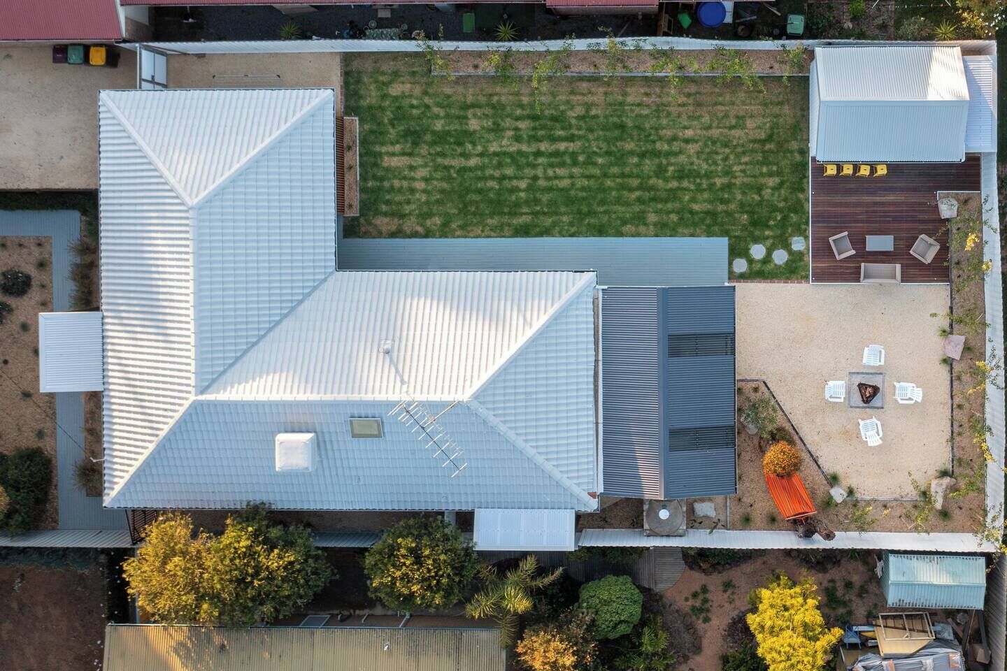An aerial view of a building with a sloped roof, a patio area with outdoor seating, and a small garden.