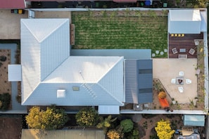 An aerial view of a building with a sloped roof, a patio area with outdoor seating, and a small garden. - Ocean Breeze Retreat (Ocean Grove)