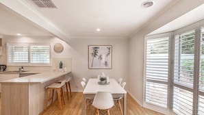 A modern kitchen with a central island, wooden chairs, and a dining table. - Ocean Breeze Retreat (Ocean Grove)