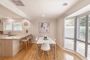 A modern kitchen with a central island, wooden chairs, and a dining table. - Ocean Breeze Retreat (Ocean Grove)
