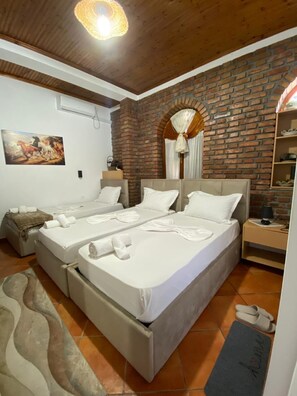 Habitación de hotel con dos camas, una pared de ladrillo, un cuadro y techo de madera.
