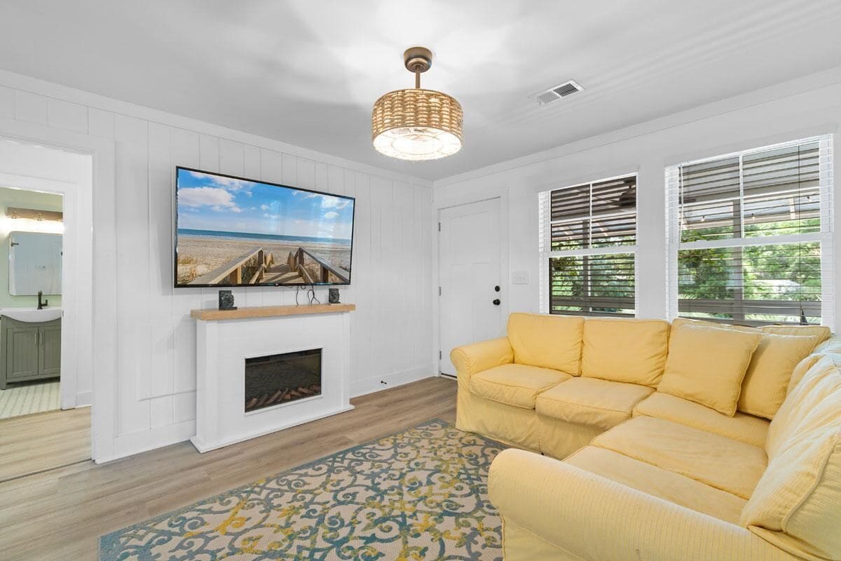 A living room with a television mounted above a fireplace, a yellow sofa, and a patterned rug.
