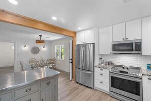 A modern kitchen with white cabinetry, stainless steel appliances, and a wooden ceiling beam. - Sea Turtle Lowcountry Retreat (Pawleys Island)