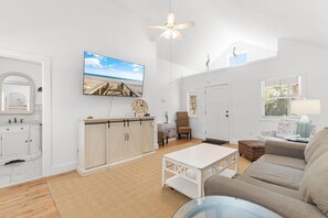 A spacious living room with a white sofa, a coffee table, and a television mounted on the wall. - Sea Turtle Lowcountry Retreat (Pawleys Island)