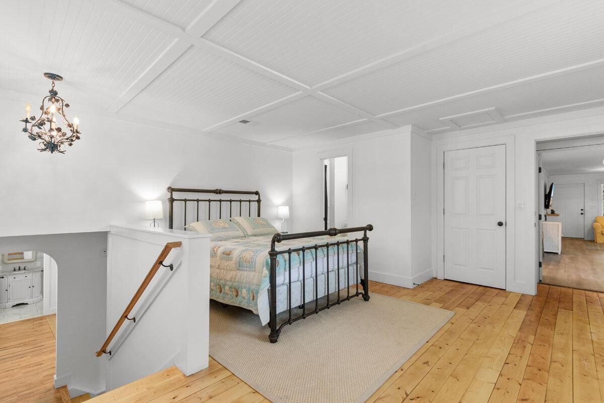 A bedroom with a bed, a chandelier, a staircase, and a door leading to another room.