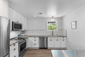 Eine moderne Küche mit weißen Schränken, Edelstahlgeräten und einem Fenster mit Blick auf Grünflächen.