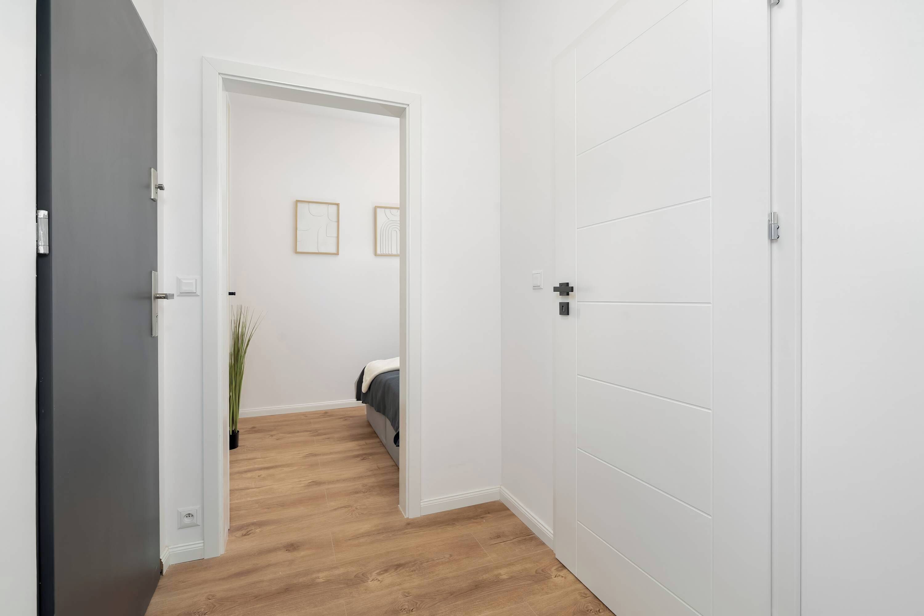 Un pasillo con piso de madera, una cama con cabecera blanca y dos cuadros en la pared.